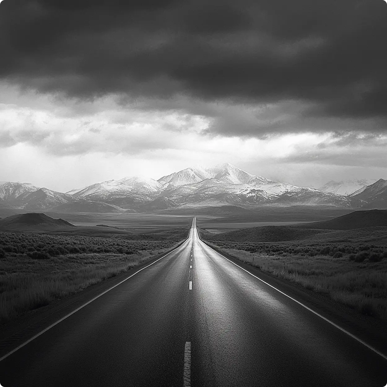 A paved road with fields on the sides leading to a mountain range
